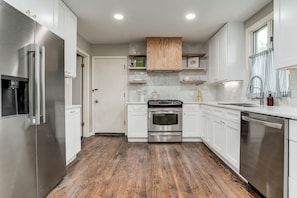 Eine moderne Küche mit weißen Schränken, einem Edelstahlkühlschrank, einem Backofen und einem Geschirrspüler.
