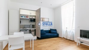 Moderni olohuone, jossa on ruokailutila, pieni keittiö, sohva ja televisio.