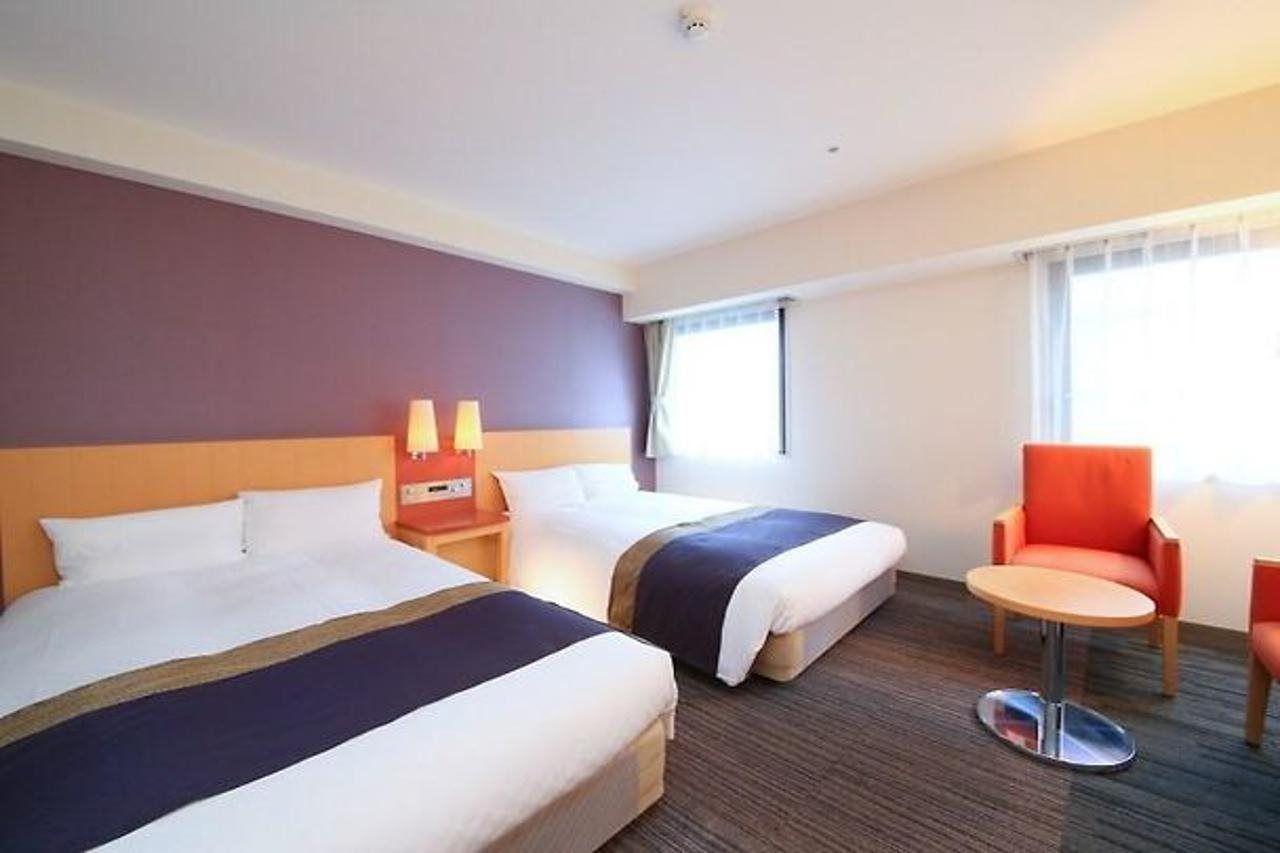 Habitación de hotel con dos camas, una mesita redonda y una sola silla.