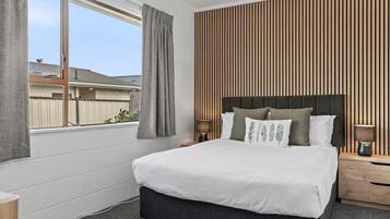 A bedroom with a bed, two bedside tables, a window with curtains, and a wooden slat wall.