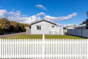 Un bâtiment d’un seul étage, à l’extérieur blanc, avec un petit porche et une clôture en bois peinte en blanc à l’avant.