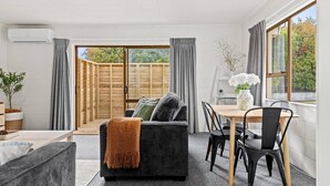 A modern living room with a sofa, a dining table, and chairs. There is a sliding glass door leading to an outdoor area. - Cozy Retreat 2 - modern townhouse living (Taupō)