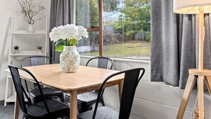 A dining area with a wooden table, black chairs, a white vase with flowers, and a view of greenery outside. - Cozy Retreat 2 - modern townhouse living (Taupō)