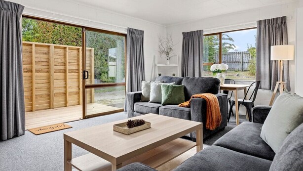 A modern living room with a sofa, coffee table, and a dining area with chairs. - Cozy Retreat 2 - modern townhouse living (Taupō)