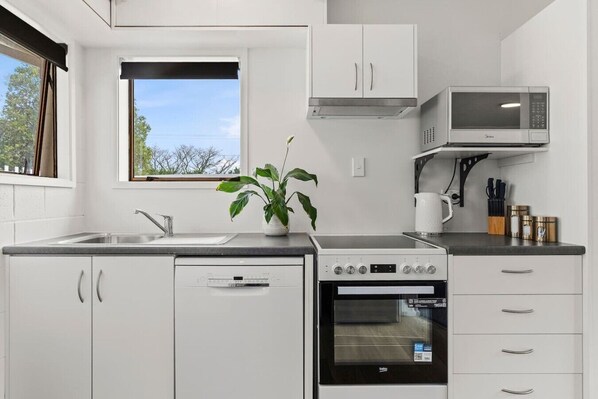 A modern kitchen with white cabinetry, a built-in microwave, an oven, and a window with a view of trees.