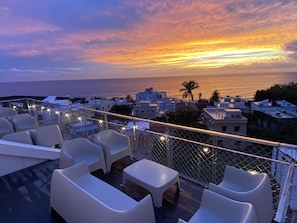 A rooftop terrace with white plastic chairs and tables, overlooking a coastal town at sunset. - Hayata Hotel No Children Under 12 Years Old (Hengchun)
