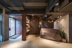 A modern reception area with a geometric reception desk, a bookshelf, and a wall with hanging lights. - Hayata Hotel No Children Under 12 Years Old (Hengchun)
