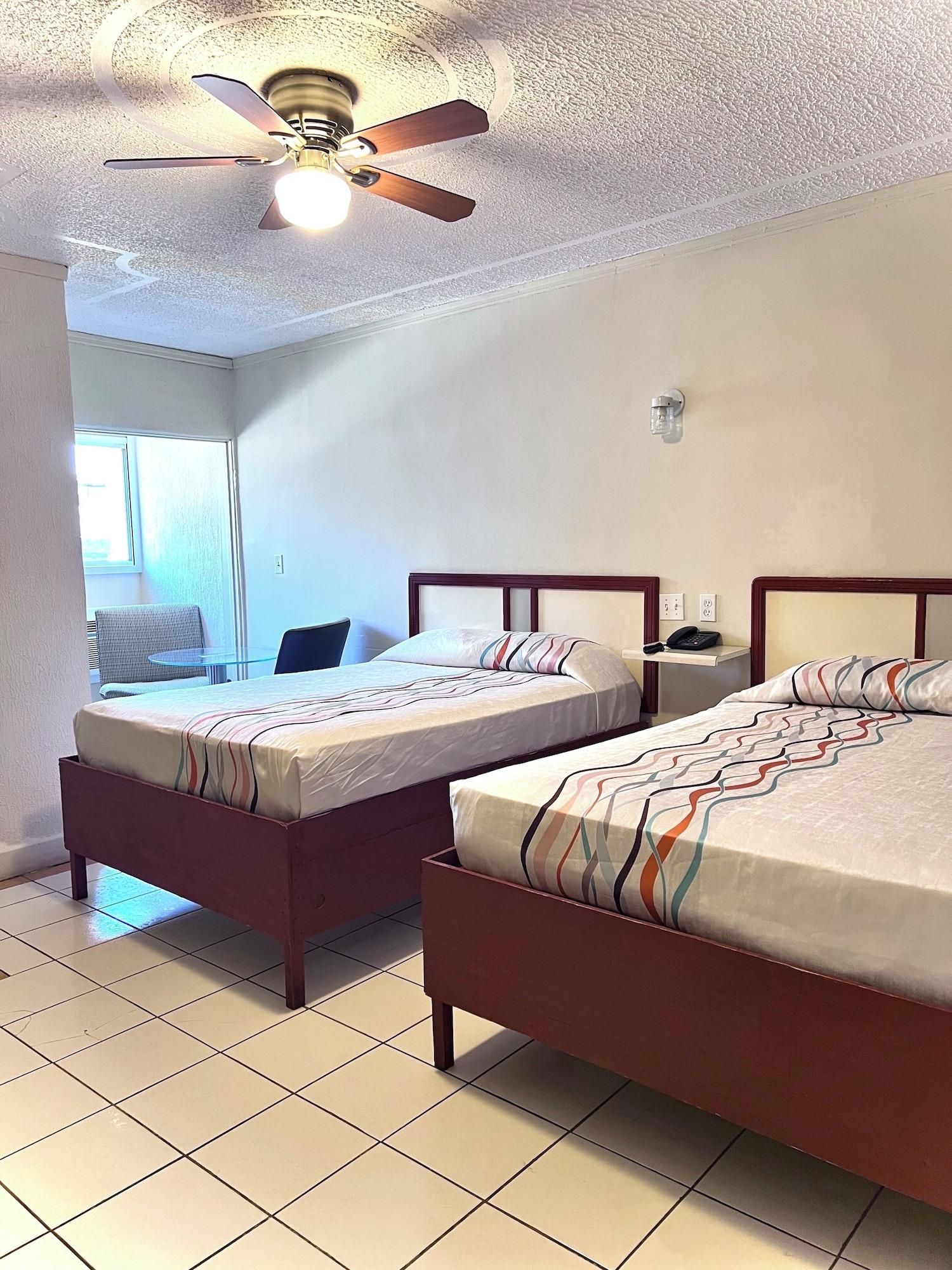 A hotel room with two beds, a ceiling fan, a window, and a chair.