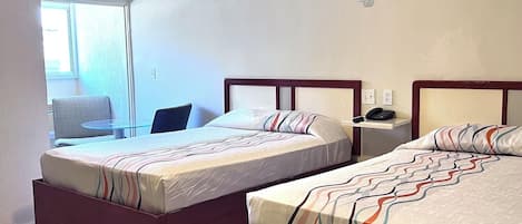 A hotel room with two beds, a ceiling fan, a window, and a chair.