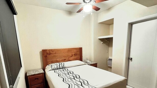 A bedroom with a bed, a nightstand, a ceiling fan, a door, and a tiled floor. - Hotel Lea N (Tijuana)