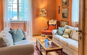 Una sala de estar acogedora con un revestimiento de madera, un sillón rojo, un sofá blanco y una mesa de centro de cristal.