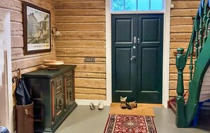 Un interior de madera con una puerta oscura, un mueble pequeño, una alfombra y un gato en el suelo.