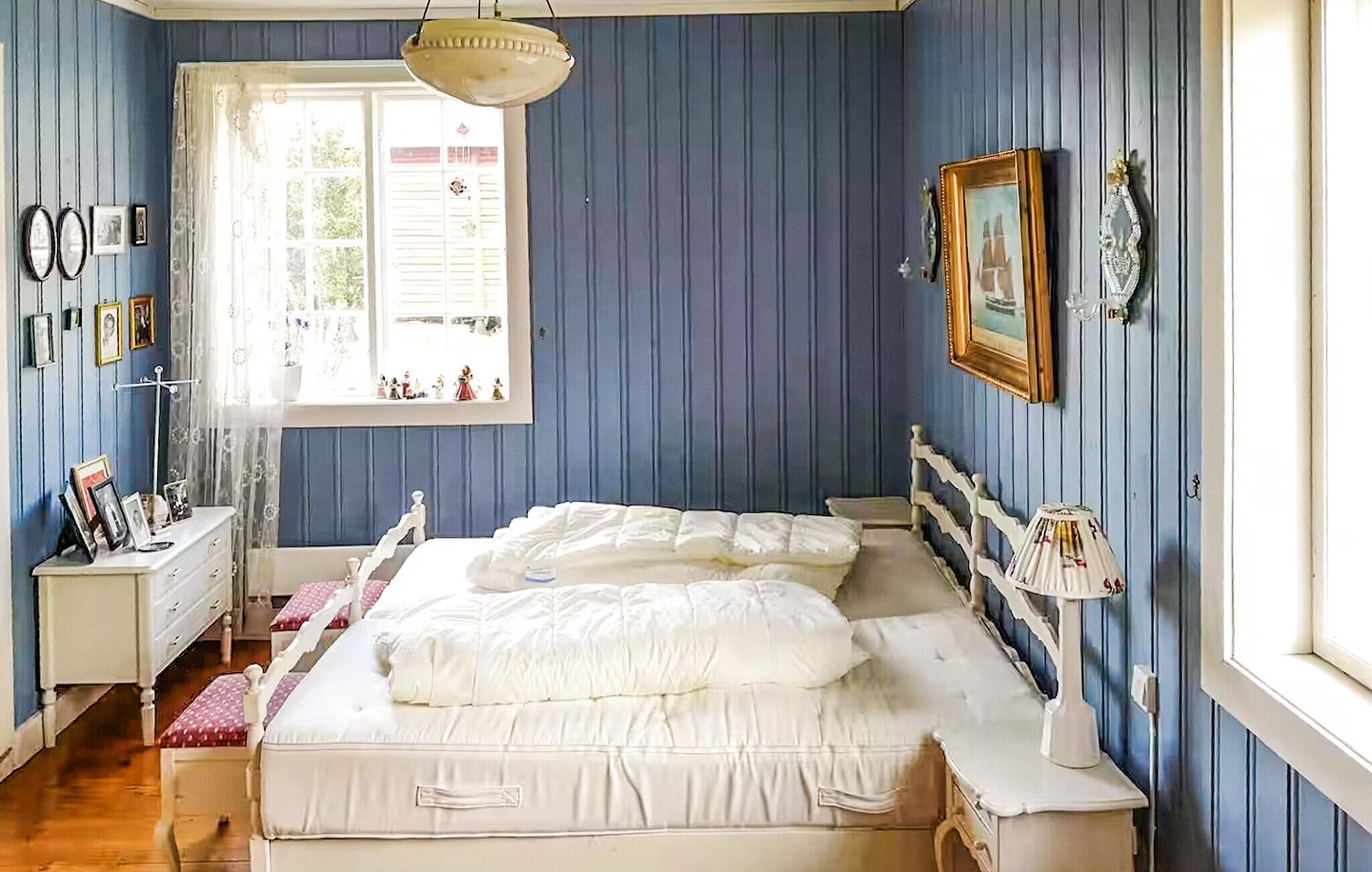 Ein Schlafzimmer mit zwei Betten, einem Fenster mit Vorhängen, einem Nachttisch und Wanddekorationen.