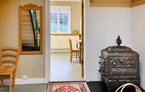 Una habitación con una silla de madera, un tapete estampado, una estufa antigua y vistas a una cocina con ventana.