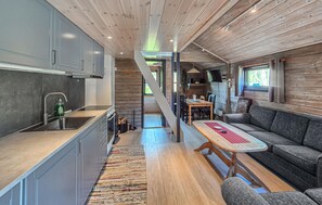 Eine moderne Küche mit eingebautem Herd, ein Essbereich mit Holztisch und Stühlen und eine gemütliche Sitzecke mit einer Couch.