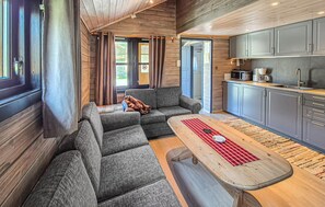 Ein gemütlicher Wohnbereich mit einer Couch, einem Holztisch und einer Küche mit grauen Schränken.
