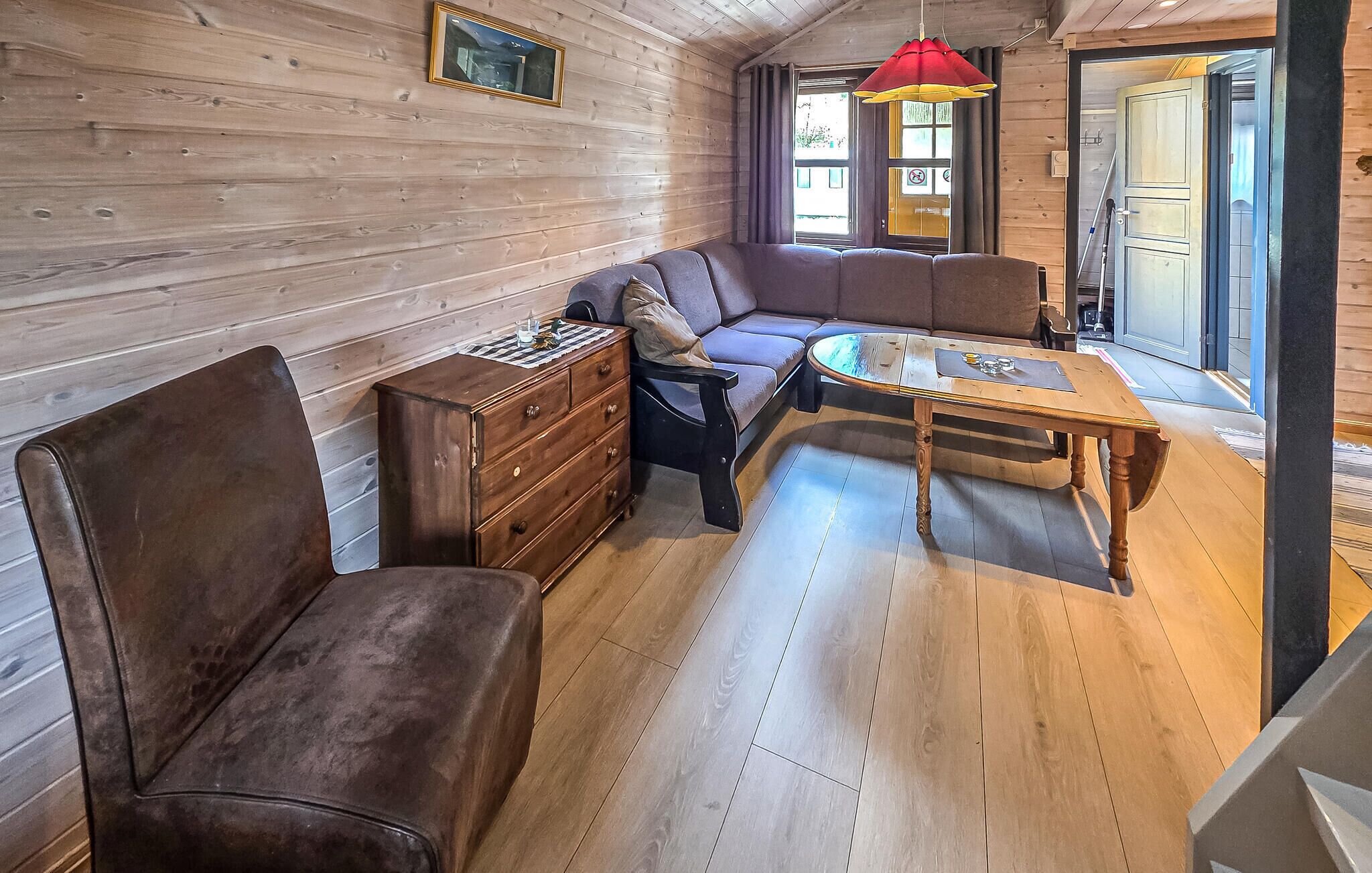 A wooden interior with a sofa, a wooden table, a dresser, and a red hanging light fixture.