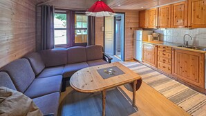 L’intérieur chaleureux d’un chalet comprend un canapé, une petite table en bois, un coin cuisine avec des meubles en bois et un luminaire rouge suspendu.