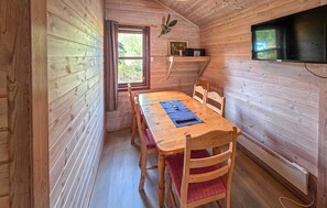 A wooden interior with a dining table, chairs, a TV mounted on the wall, and a window with a view of greenery. - Cozy home in Tjørhom with sauna (Tjørhom)