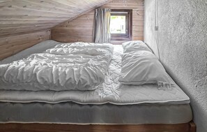 A single bed in a room with wooden walls and a sloped ceiling, a window with curtains, and a textured wall on the right. - Cozy home in Tjørhom with sauna (Tjørhom)