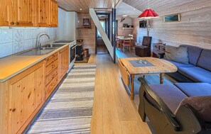 A compact kitchen with wooden cabinets, a sink, and a stove. There's a dining area with a table and chairs, and a sofa. - Cozy home in Tjørhom with sauna (Tjørhom)