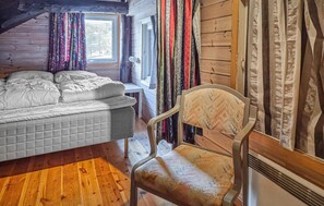 A room with a bed, a chair, wooden walls, a window, and curtains.