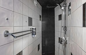 A bathroom with tiled walls, a glass shower enclosure, and a handrail.