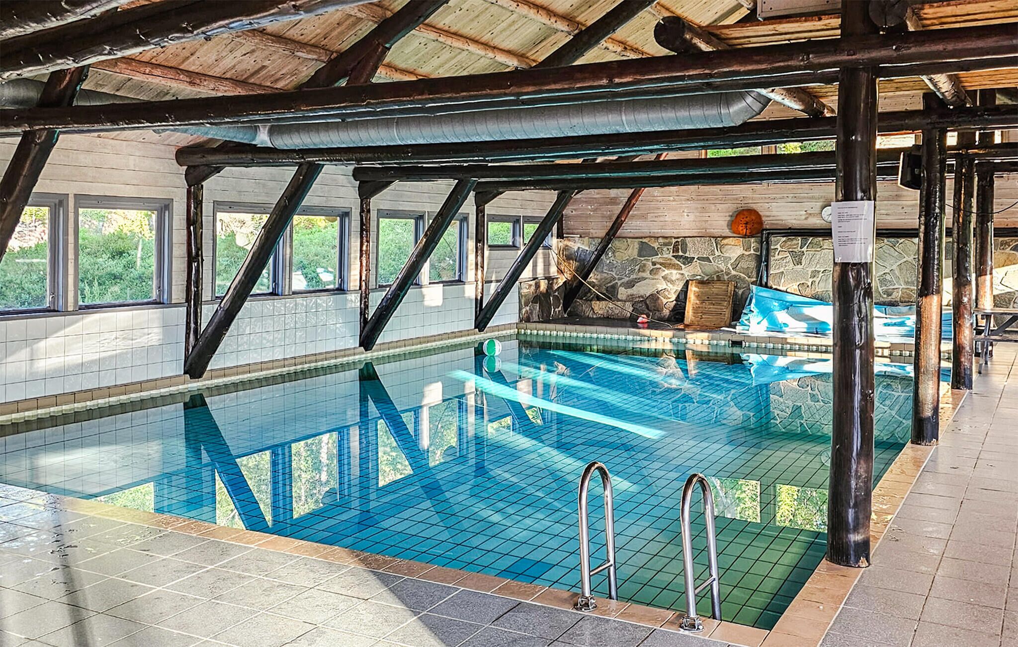 Una piscina interior con agua cristalina, rodeada de paredes de piedra y vigas de madera.