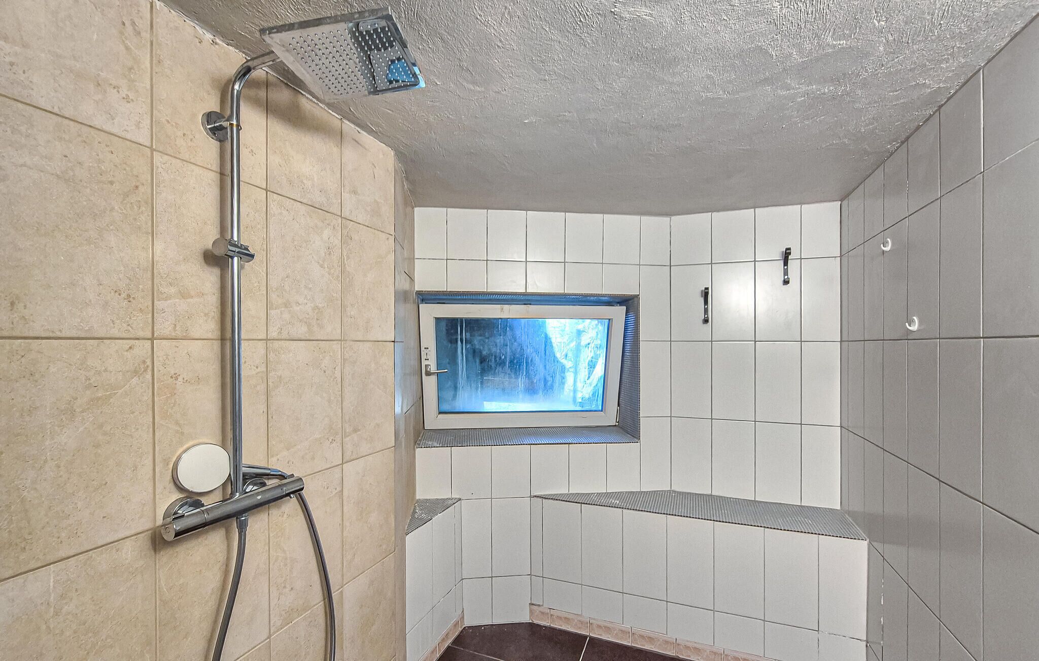 Une douche équipée d’un pommeau de douche à main, d’une fenêtre et de murs carrelés.