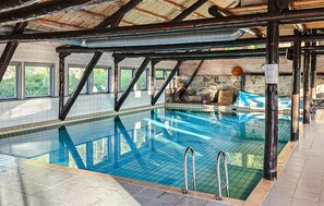 An indoor swimming pool with clear water, surrounded by stone walls and wooden beams.