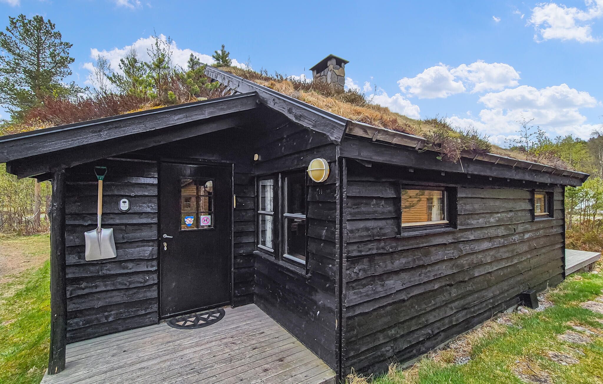 Une cabane rustique en rondins de bois, dotée d’une porte d’entrée, d’une fenêtre et d’un petit porche.