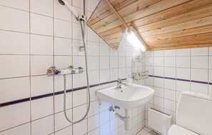 Un baño con azulejos blancos, techo de madera, un lavamanos, un inodoro y una ducha.