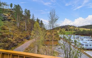 Paisaje montañoso con una terraza de madera que da vista a un estacionamiento con vehículos recreativos.