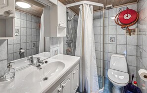 A bathroom with a sink, toilet, shower curtain, and a red hose.