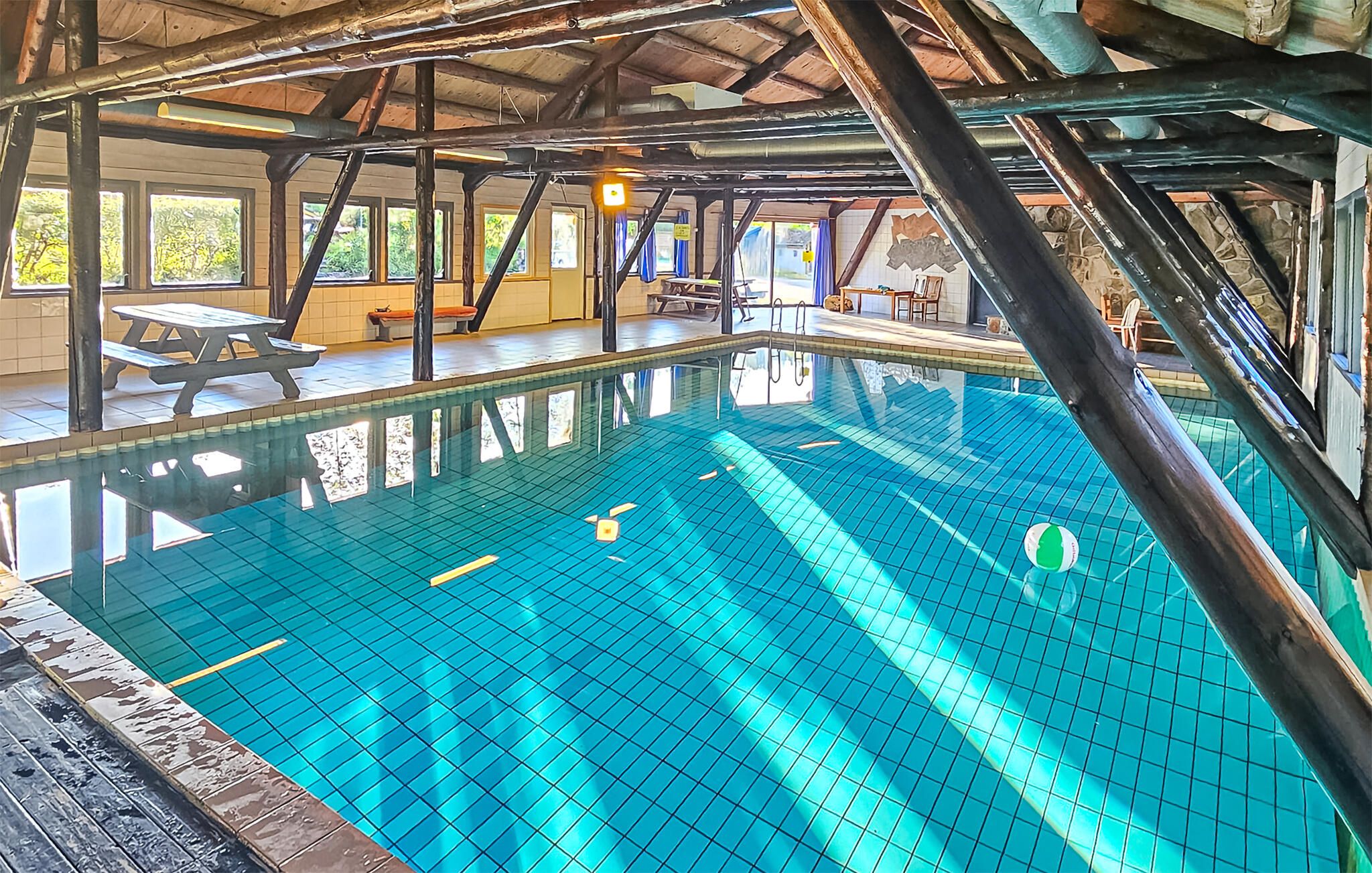 An indoor swimming pool with a tiled floor, wooden beams, and a picnic table.