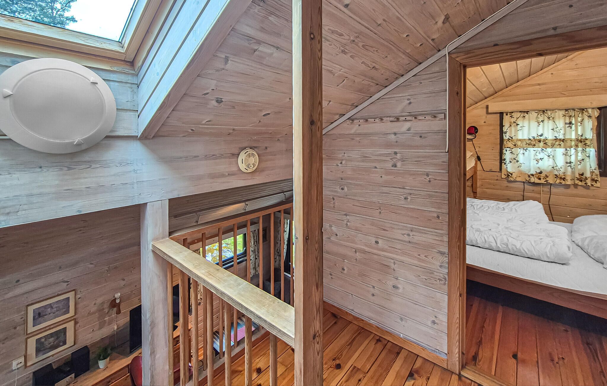 L’intérieur d’une cabane en bois, avec une chambre à coucher située en mezzanine, un escalier et une lucarne.