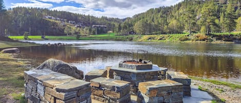 Une construction en pierre située près d’une rivière, d’où l’on a une vue dégagée sur une colline boisée en arrière-plan.