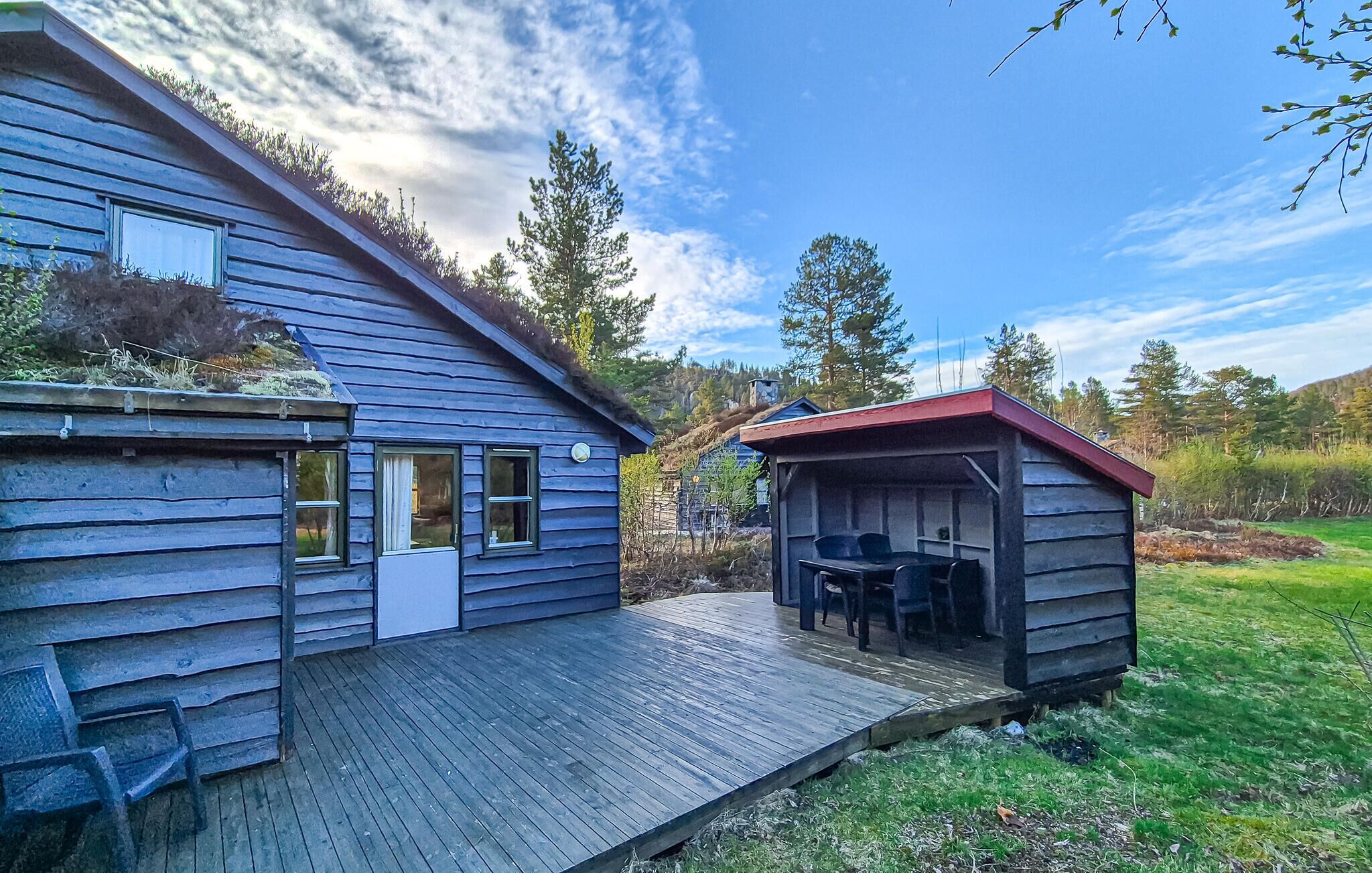 A wooden cabin with a deck, a covered outdoor seating area, and a view of the surrounding forest.