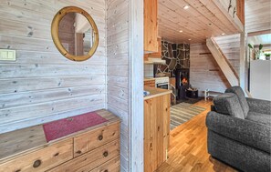 A cozy cabin interior with a wooden wall, a fireplace, a sofa, and a kitchen area. - Beautiful home in Tjørhom with sauna (Tjørhom)