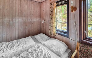 A room with wooden walls, a bed with white bedding, a window with curtains, and a wall-mounted light fixture. - Stunning home in Tjørhom with sauna (Tj ørhom)