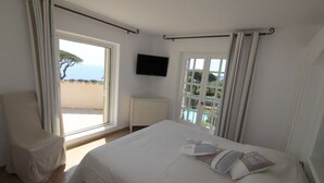 Een slaapkamer met een bed, een stoel, een televisie en een raam met gordijnen.