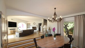 Een ruime woonkamer met een eettafel, stoelen, een kroonluchter en een open haard.