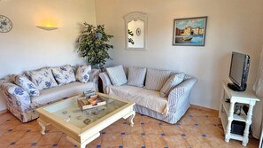 A living room with two sofas, a coffee table, a television on a stand, a wall clock, a framed painting, and a potted plant. - Apartment T4 Duplex - 6 people - Sea view - Swimming pool residence - Air conditioning - WiFi -... (STE MAXIME)