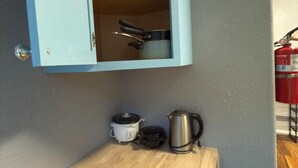 Une cuisine compacte avec un meuble bleu, un plan de travail en bois, une bouilloire et un autocuiseur.