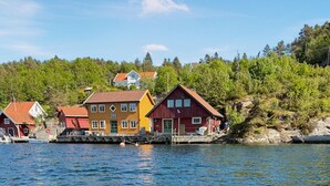 Una propiedad frente al agua con varias edificaciones, incluyendo una casa amarilla y una casa roja, cerca de una masa de agua.
