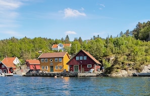 A waterfront property with multiple buildings, including a yellow house and a red house, near a body of water. - Amazing home in Mandal with house sea view (Mandal)