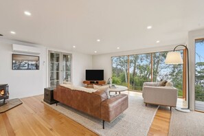 Un salon moderne doté d’une cheminée, d’un téléviseur et d’une grande fenêtre donnant sur la forêt.