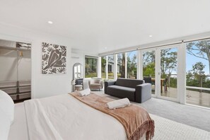 Une chambre à coucher avec un grand lit, un canapé, un fauteuil et une grande fenêtre donnant sur l’extérieur.