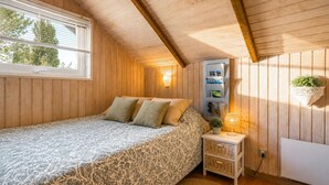 Ein Schlafzimmer mit einem Bett, einem Nachttisch, einem an der Wand befestigten Regal mit Büchern und einem Fenster mit Jalousien.