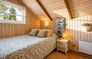 Ein Schlafzimmer mit einem Bett, einem Nachttisch, einem an der Wand befestigten Regal mit Büchern und einem Fenster mit Jalousien.